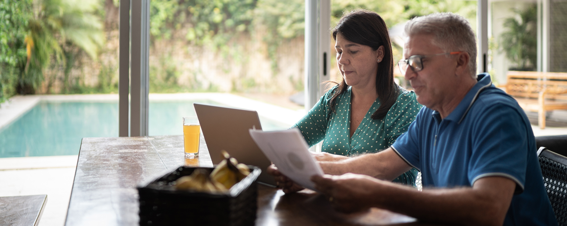 Mature couple reviewing paperwork sitting at a table in a kitchen.