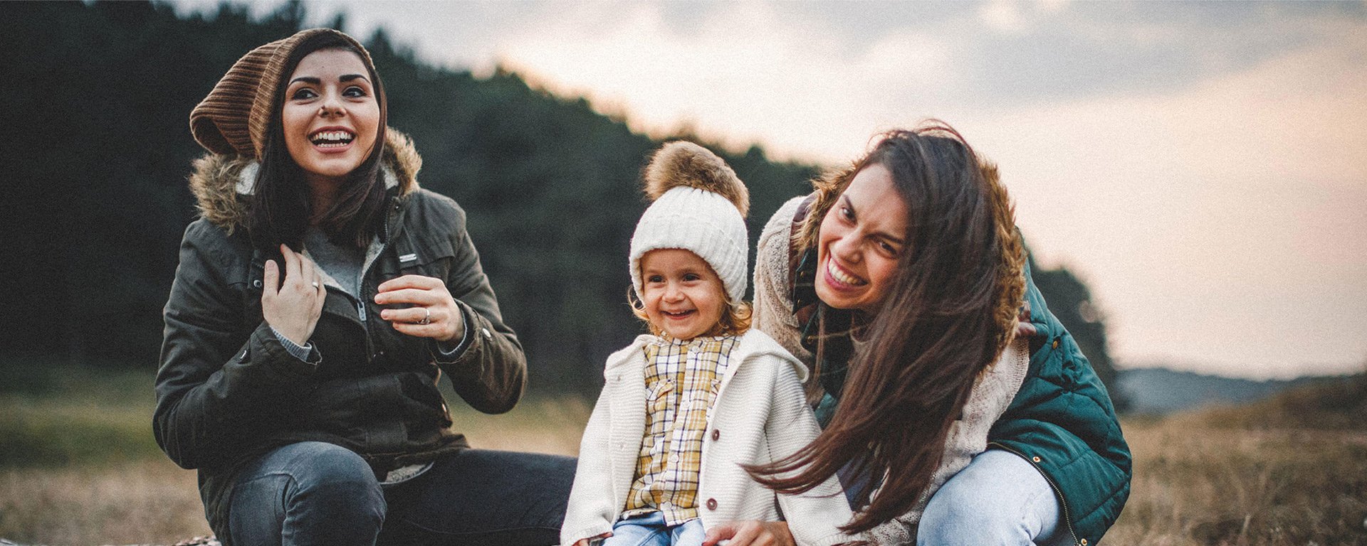 Same-sex couple enjoying nature with their toddler daughter. Wearing jackets, hats, and hiking boots. Late Autumn day.