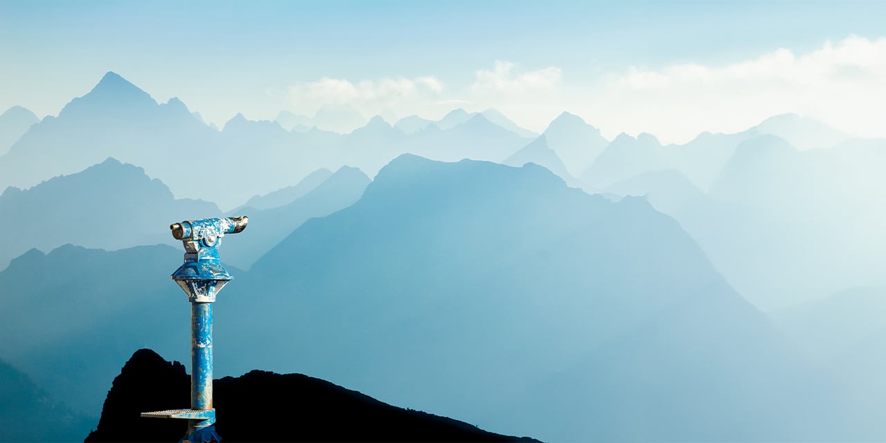 A blue telescope pointed towards a mountain skyline