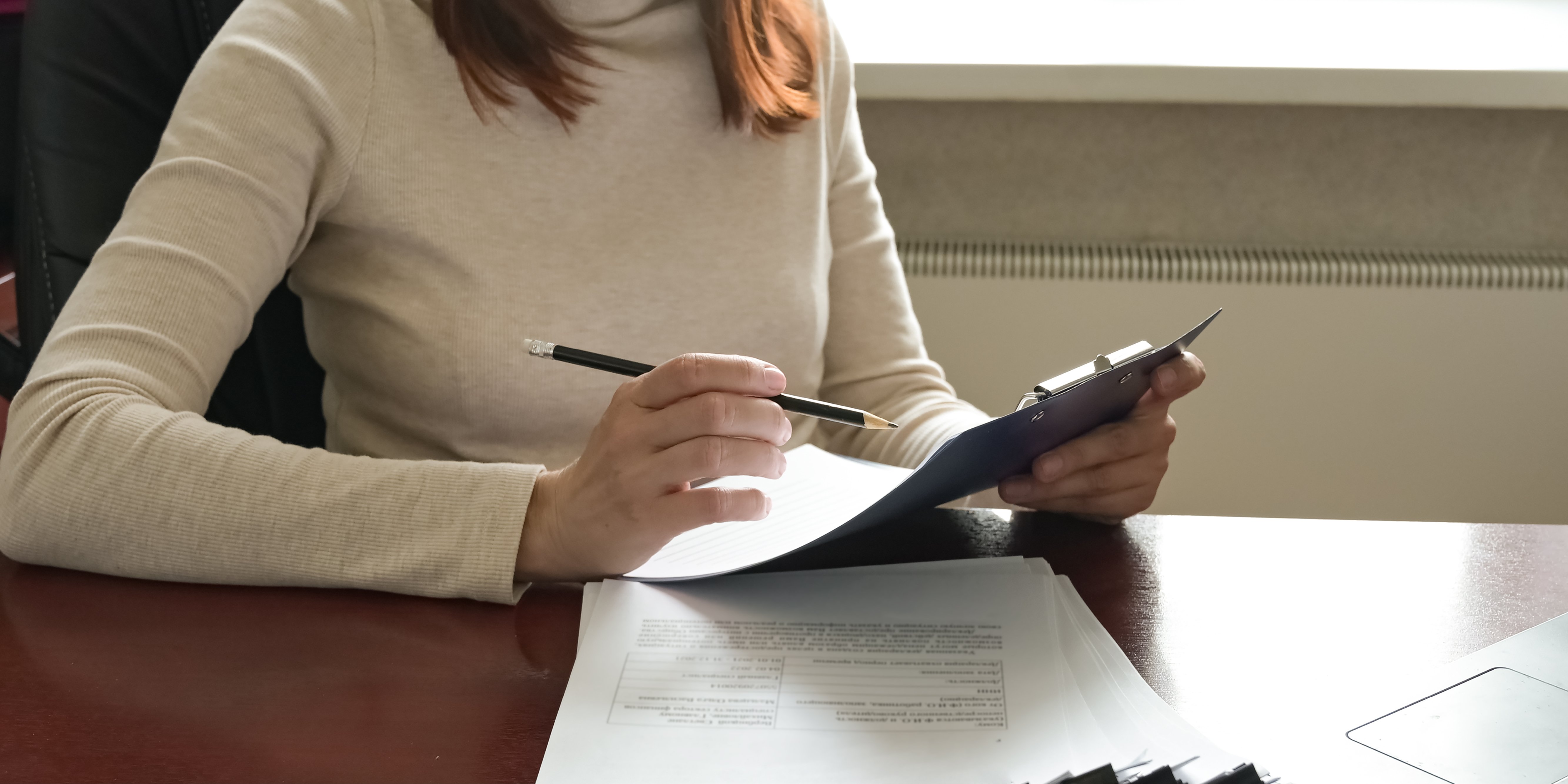 Woman holding a pen and reviewing contracts while sitting as a desk.