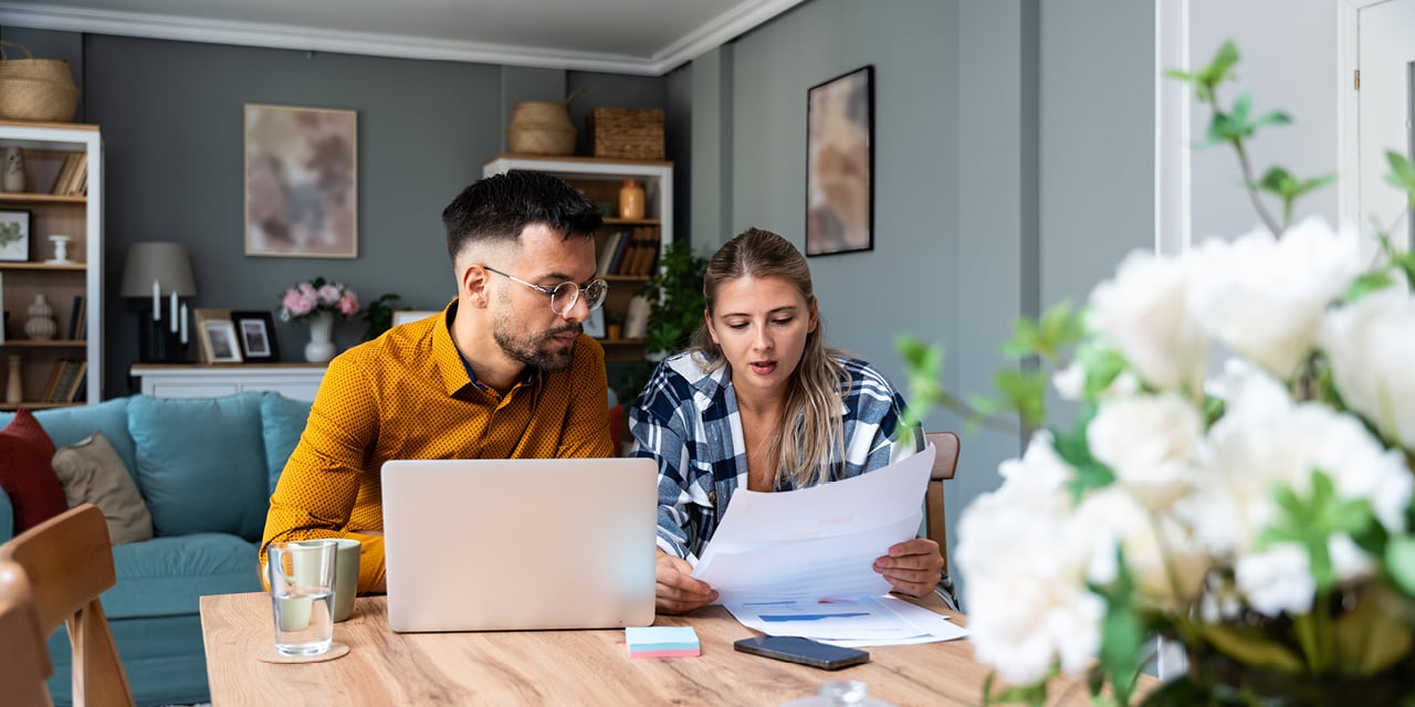 Couple sitting at table with laptop and reviewing paperwork. 