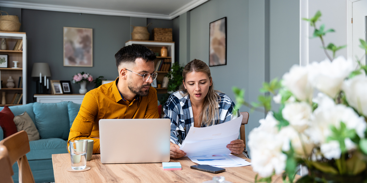 Couple sitting at table with laptop and reviewing paperwork. 