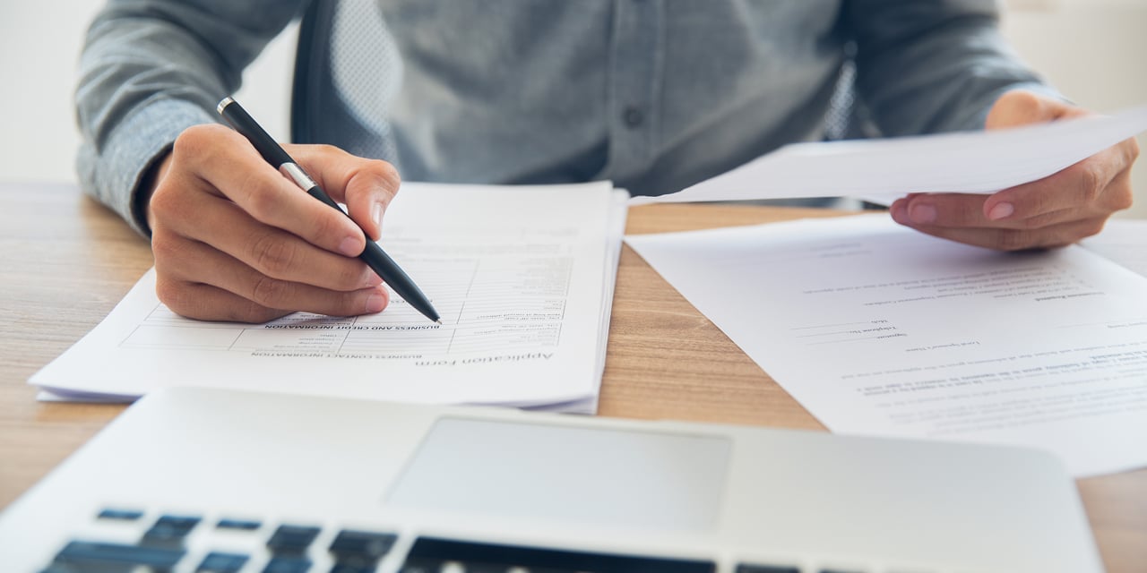 Hands holding a pen and paperwork while sitting at a table.