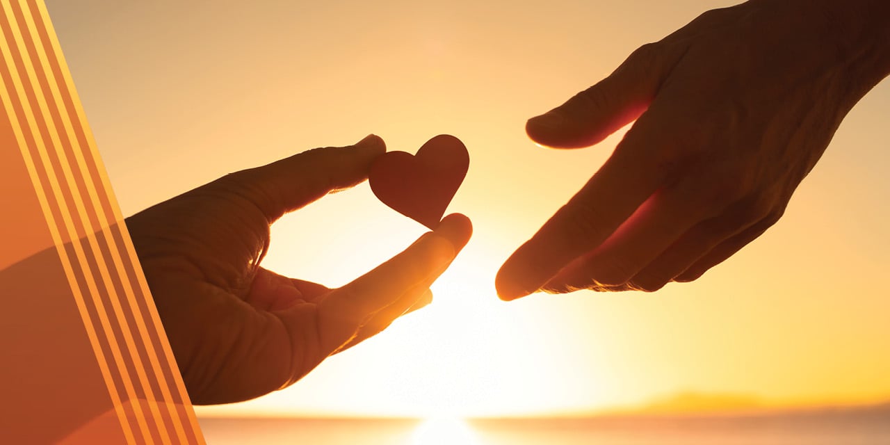 Hand holding heart with sunset in the background.