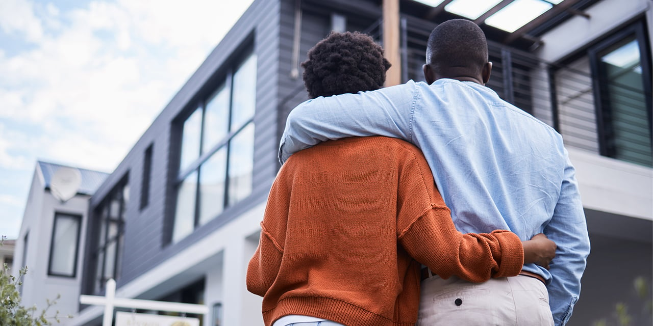 Couple standing arm in arm in front of a modern style home.