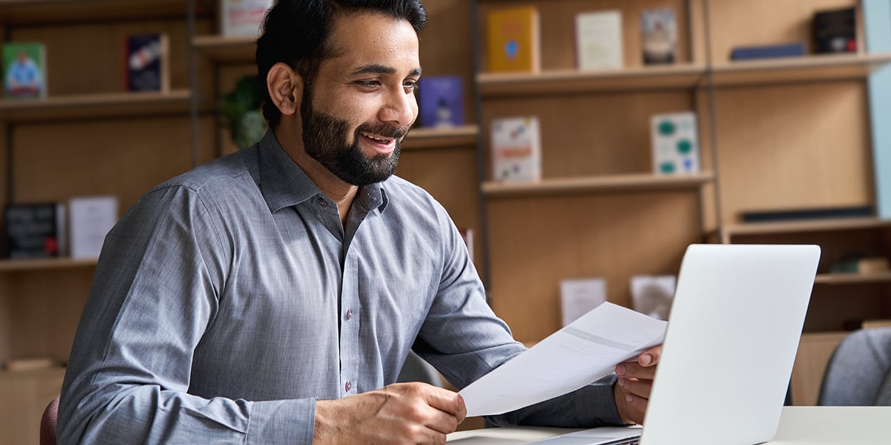 Man working on paperwork and laptop in an office environment.