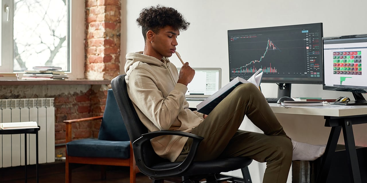 Student reading a text book while sitting in front of a computer and desk.