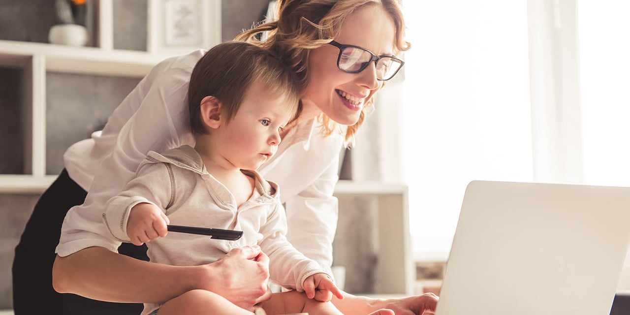 Woman with toddler sitting on table in front of a laptop computer.