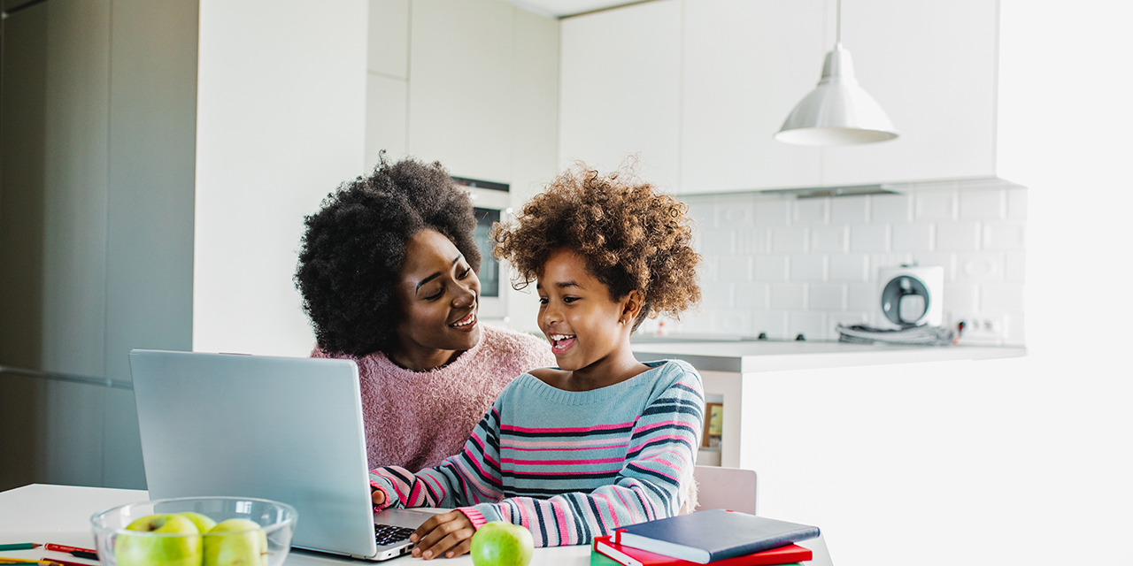 Parent and child sitting at table with laptop.