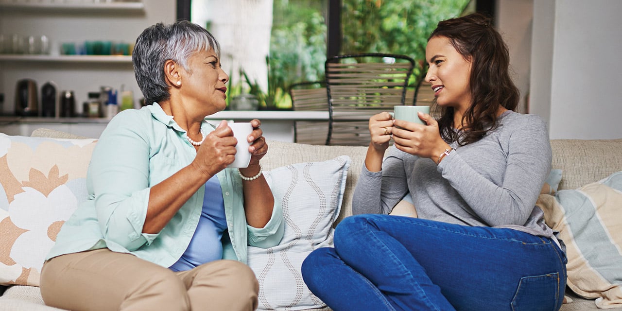 Mom and daughter sitting on sofa talking and drinking coffee.