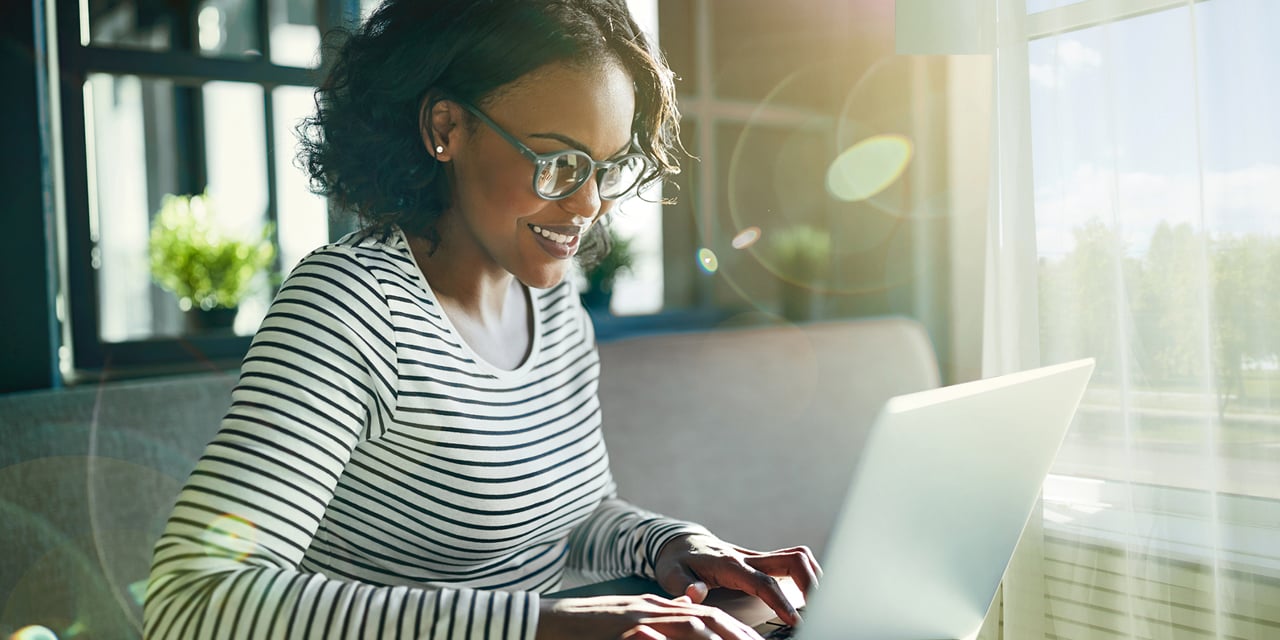 Young woman smiling and working on a laptop computer in the morning sunshine.