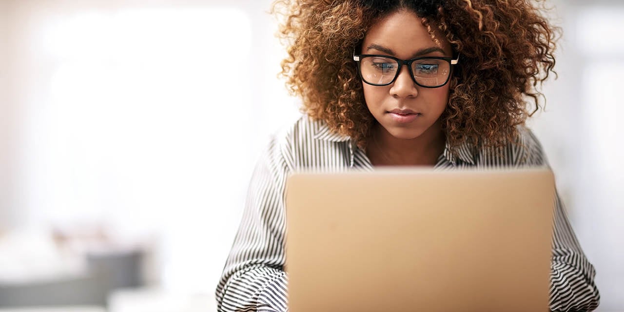 Woman wearing glasses sitting down working on a laptop.