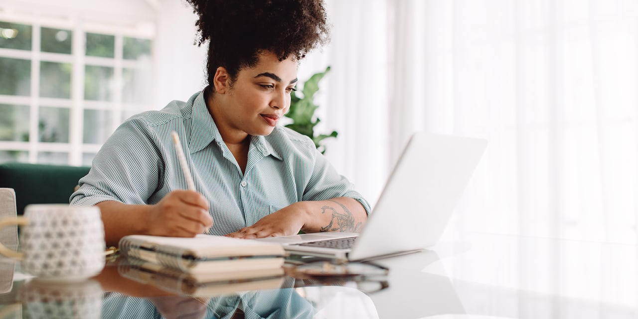 Woman doing paperwork at a computer sitting at a table.