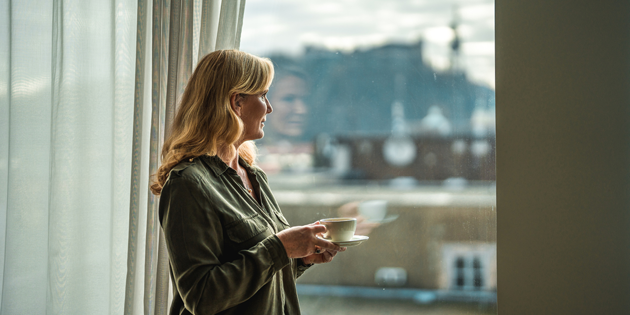 Woman holding a coffee cup while looking out a window.