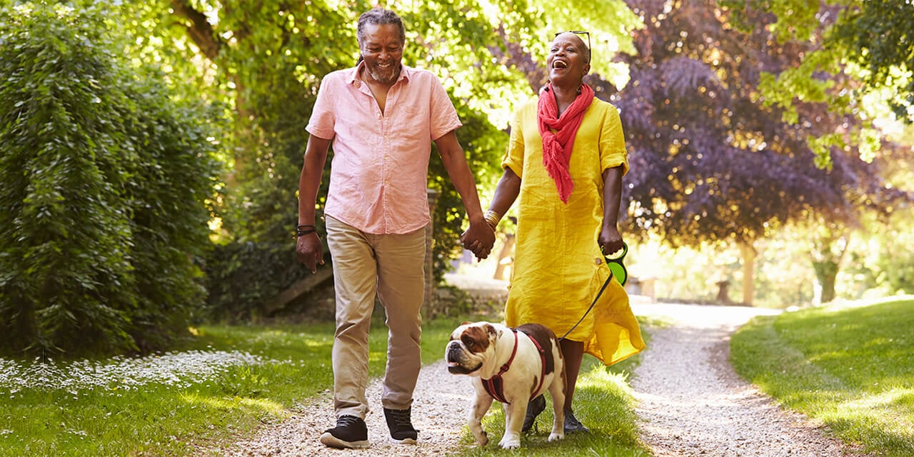 Middle aged couple walking a dog down a gravel path