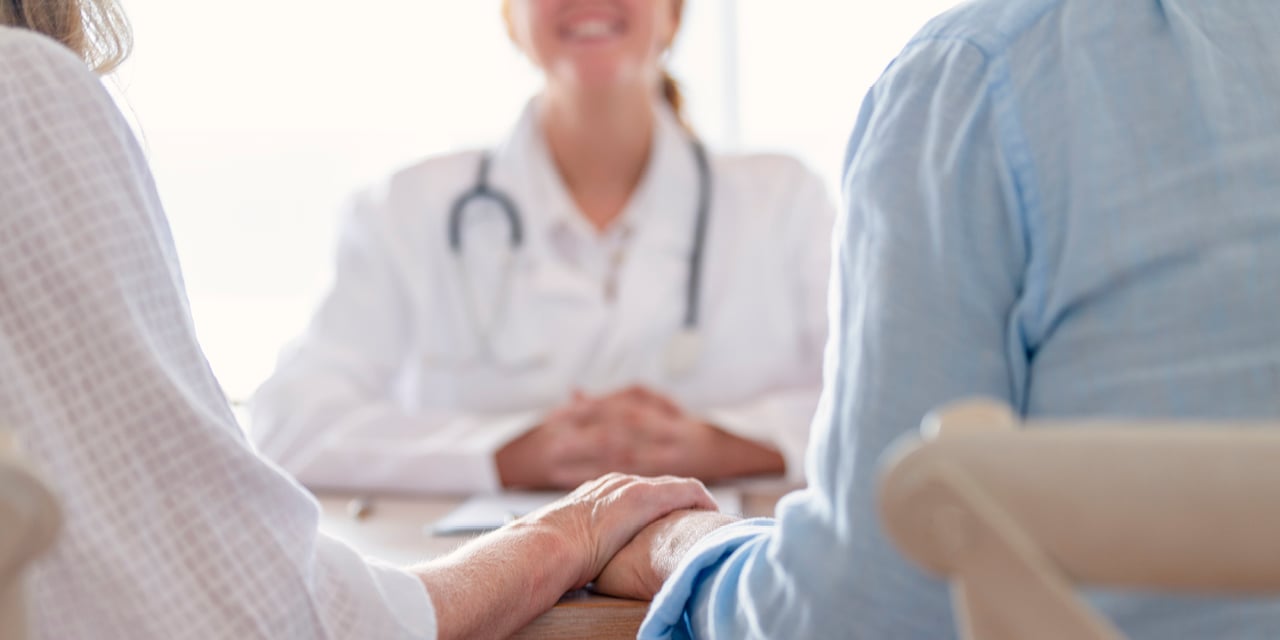 Retired couple holding hands while meeting with a doctor.