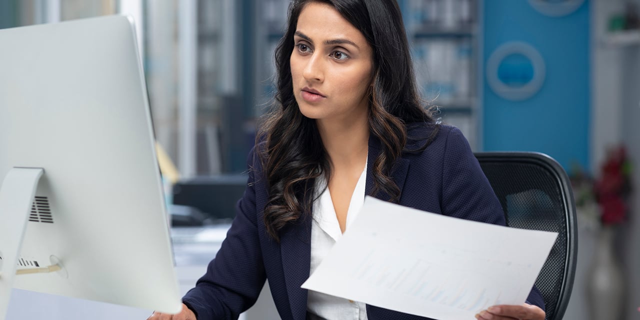 Professional woman reviewing documents while at a computer.