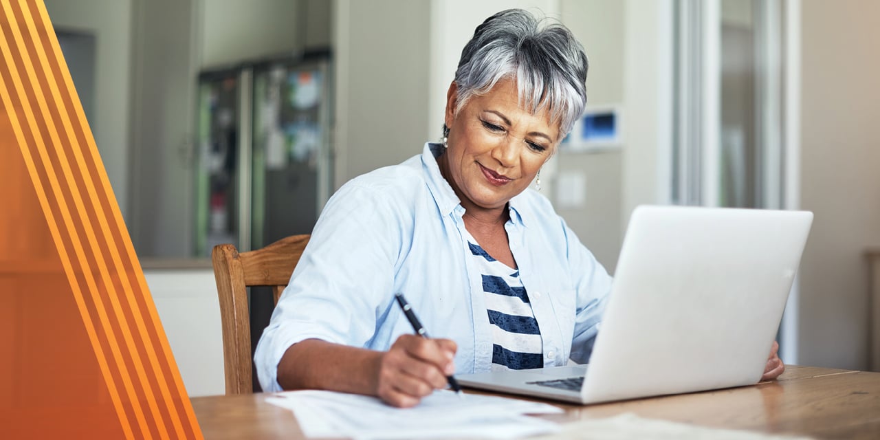 Woman reviewing paperwork sitting at a table with a laptop