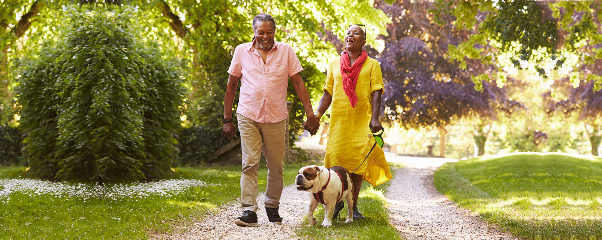 Middle aged couple walking a dog down a gravel path