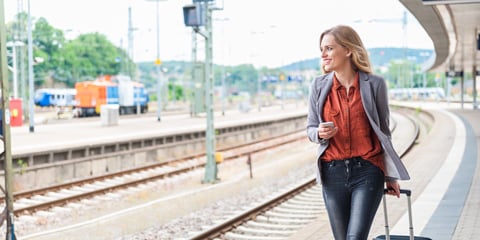 Woman talking next to train tracks with a suitcase.