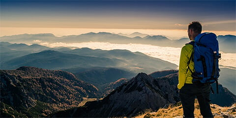 Man hiking stops to look at view at the top of a mountain.