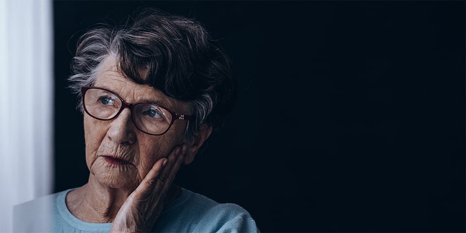 Worried, elderly woman with hand on face peering off into the distance.