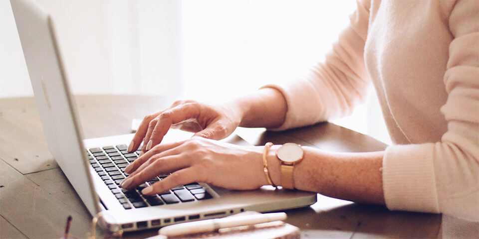 Pair of hands hovering over keyboard of silver laptop.