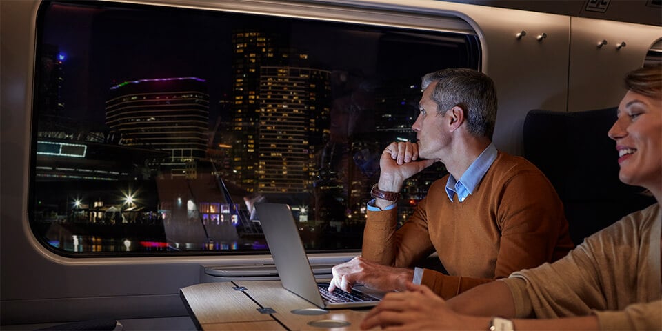 Middle-aged couple on a train at nighttime. Male is looking thoughtfully out the window.