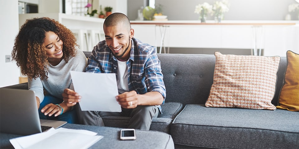 Young couple looking over documents in front of laptop on couch.