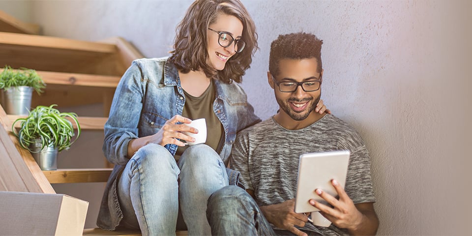 Young couple sitting on stairs looking at tablet screen. 