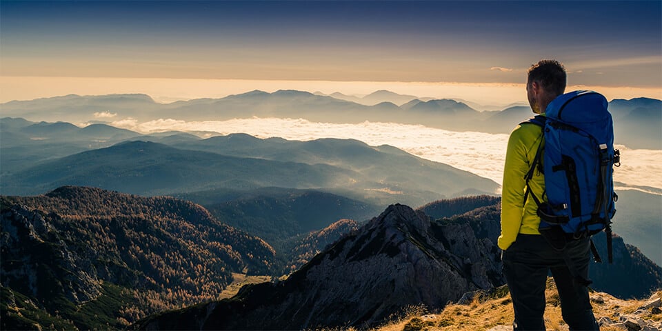 Man hiking stops to look at view at the top of a mountain.