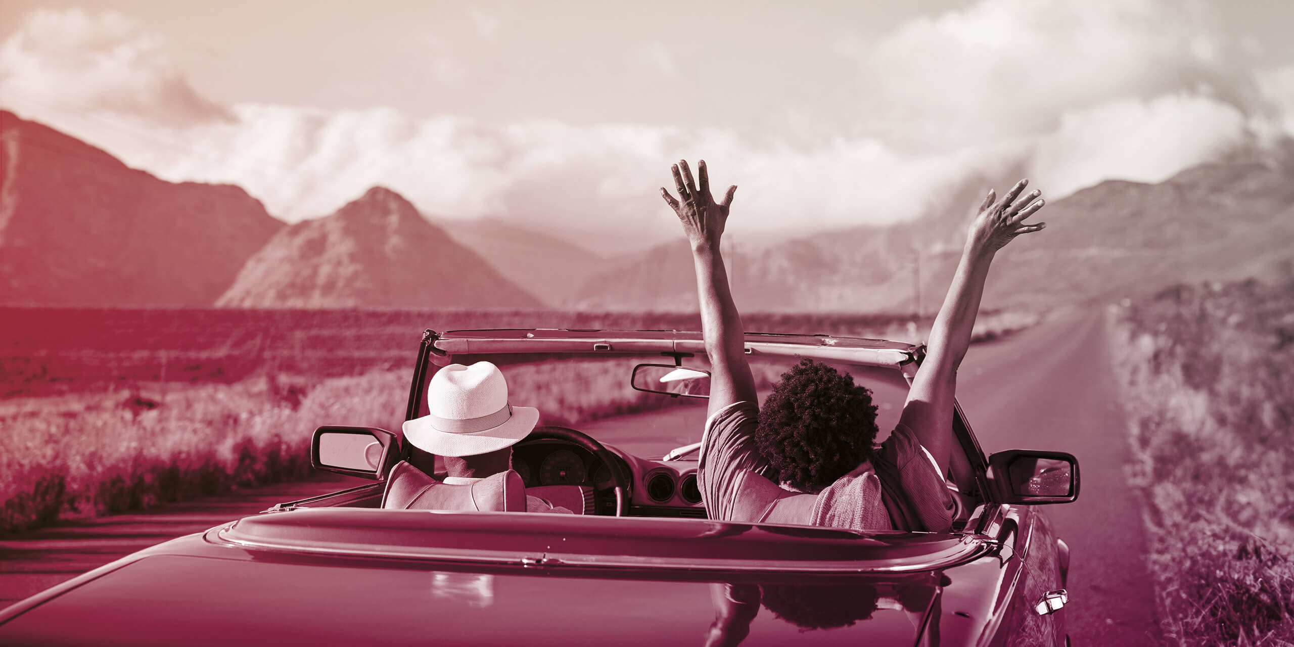 Couple driving in a convertible with passenger hands in the air