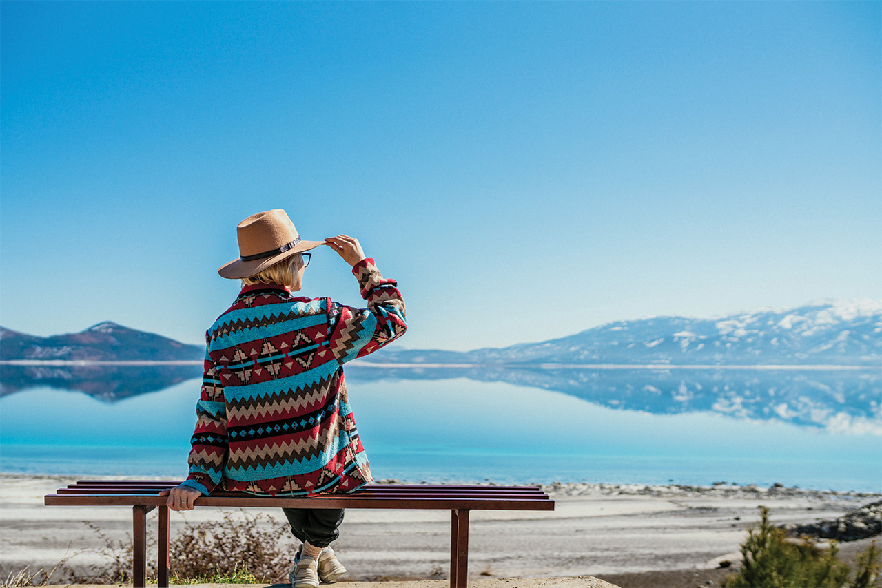 Woman sitting on a bench, looking out over a lake and mountains