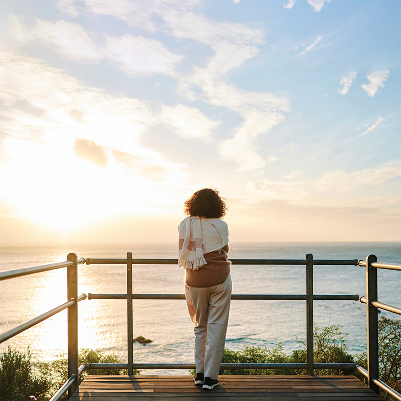 Woman standing on a pier overlooking a body of water at sunrise